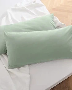 Zwei salbeigrüne Jersey-Kopfkissenbezüge liegen auf einem weißen Bettlaken.