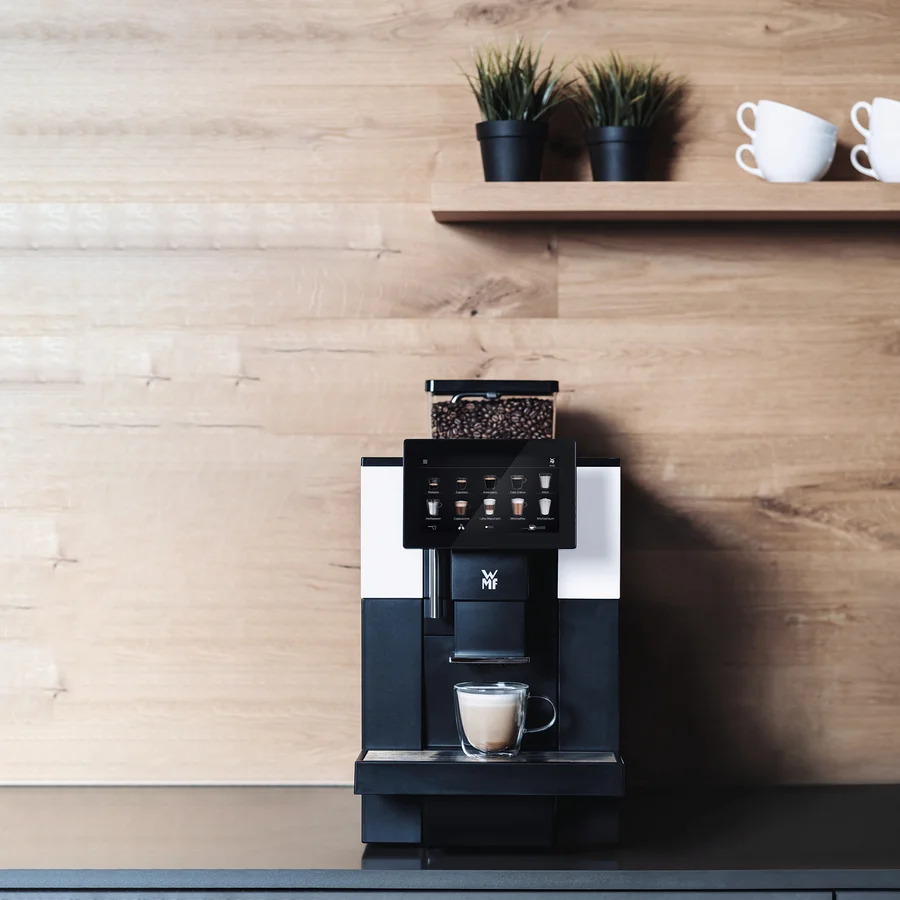 Profi-Kaffeevollautomat »WMF 950 S« vor einer Holzwand. Auf einem Regal darüber befinden sich zwei Blumentöpfe und Tassen.