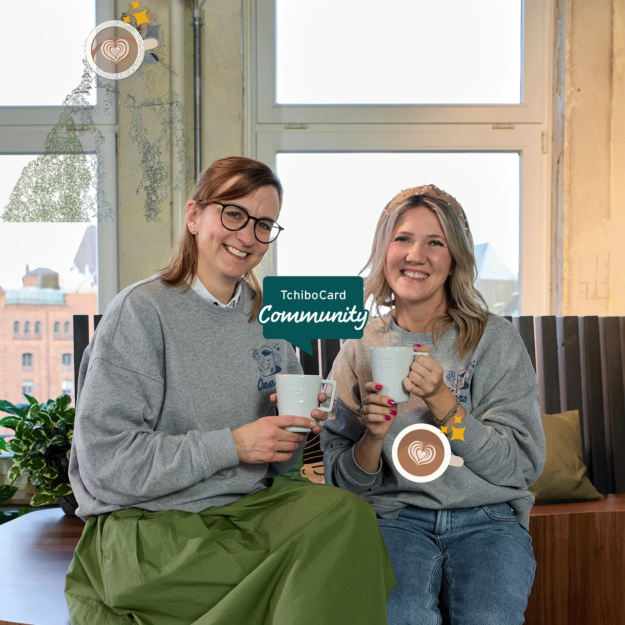 Zwei lächelnde Frauen in grauen Pullovern halten Tassen. Eine trägt einen grünen Rock und Brille, die andere Jeans. Eine Grafik mit einer Kaffeetasse mit Herz-Latte Art und dem Text „TchiboCard Community“ überlagert das Bild, alles mit Pixeleffekt.