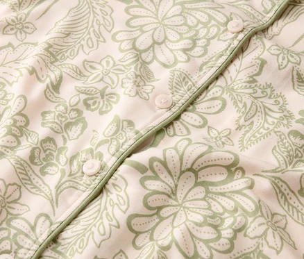 Nahaufnahme eines hellrosa Stoffes mit grünem Blumenmuster und Knöpfen.
