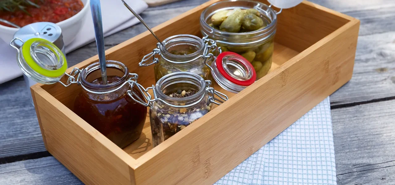 Auf einem Holztisch steht ein Tablett mit kleinen Gläsern mit verschiedenen Lebensmitteln, daneben eine Schüssel mit Soße, Fleisch, Eier und Brot.