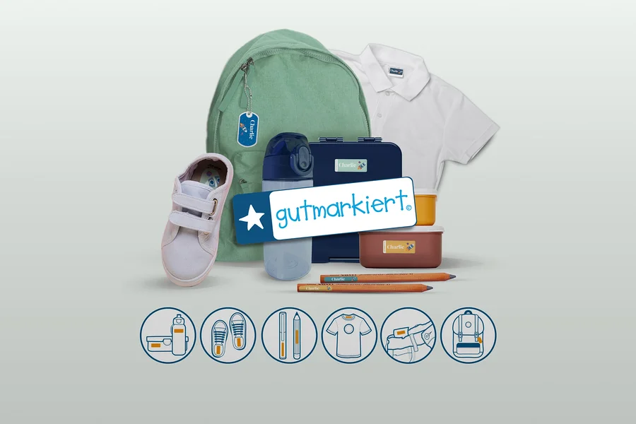 Verschiedene Schulartikel wie ein grüner Rucksack, ein weißer Schuh, eine blaue Trinkflasche, zwei Brotdosen, zwei Bleistifte und ein weißes Poloshirt sind mit personalisierten „Charlie“-Etiketten versehen. Ein „gutmarkiert.“-Logo ist mittig platziert, darunter zeigen Symbole Anwendungsbeispiele für Etiketten.
