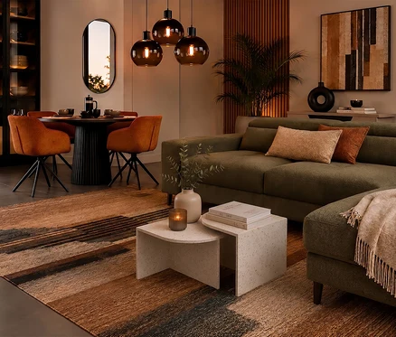 Modernes Wohn- und Esszimmer mit olivgrünem Ecksofa, schwarzem Esstisch und orangefarbenen Stühlen. Über dem Tisch hängen drei dunkle Pendelleuchten, und ein gemusterter Teppich bedeckt den Boden.