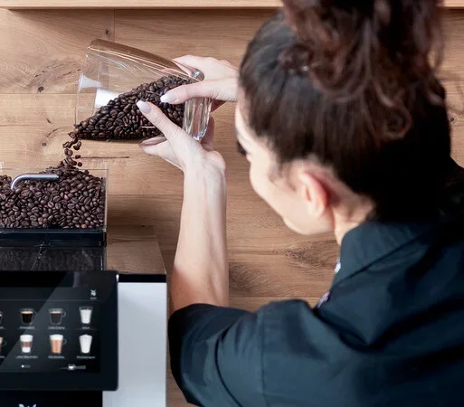 Frau füllt Kaffeebohnen in einen Profi-Kaffeevollautomat »WMF 950 S«.