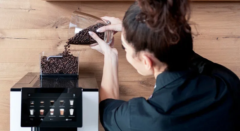 Frau füllt Kaffeebohnen in einen Profi-Kaffeevollautomat »WMF 950 S«.