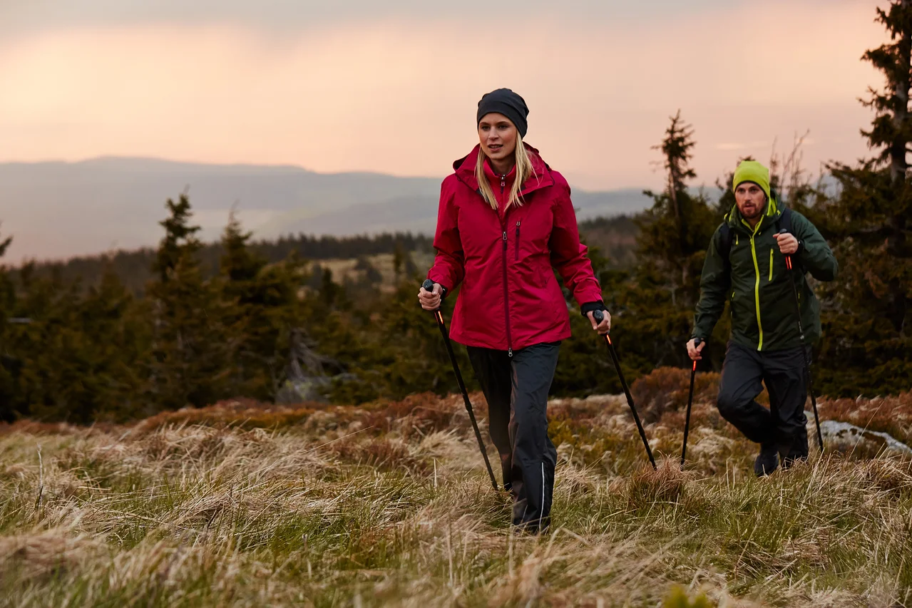 Zwei Personen wandern mit Stöcken über eine Wiese.