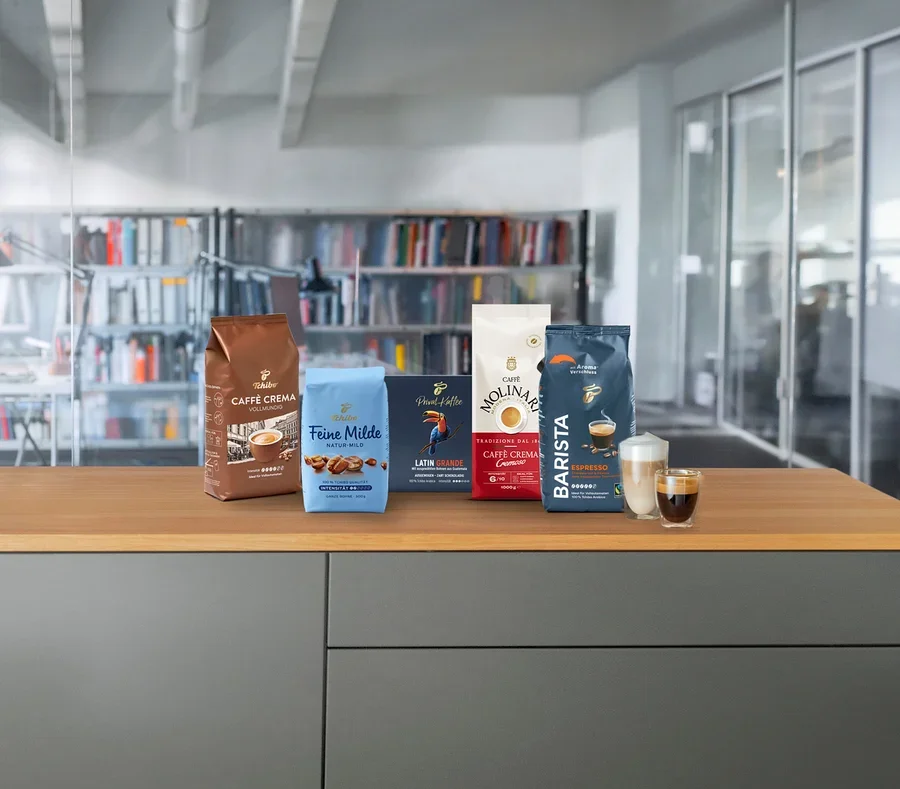Fünf Kaffeepackungen und zwei Tassen auf einer Holztheke. Von links nach rechts: Tchibo Caffe Crema, Feine Milde, Paul Möller, Cafe Molinari und Barista.