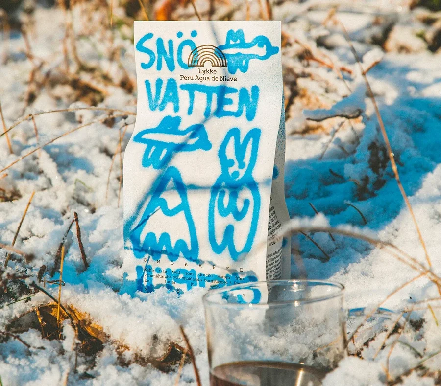 Eine Packung Lykke Peru Agua de Nieve Kaffee und ein Glas Kaffee stehen im Schnee.