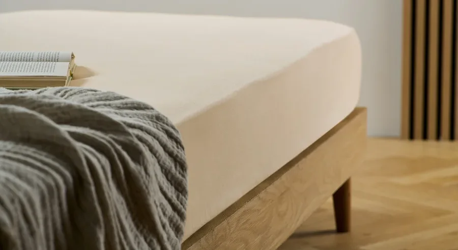 Ein cremefarbenes Biber-Spannbettlaken auf einem Bett mit einem Buch und einer grauen Decke.