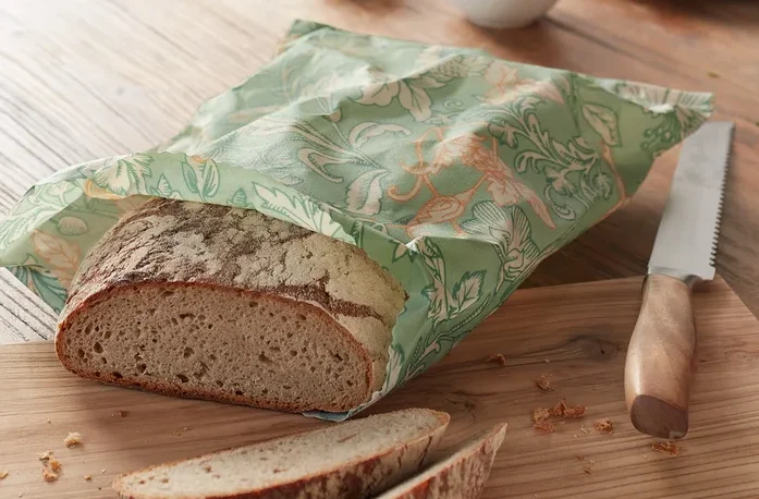 Brotlaib im Bienenwachs-Brotbeutel auf Holzbrett.