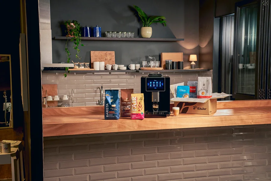 Auf einer Küchentheke stehen Kaffeebohnenpackungen und eine Tchibo-Kaffeemaschine mit einer Tasse Kaffee darunter.