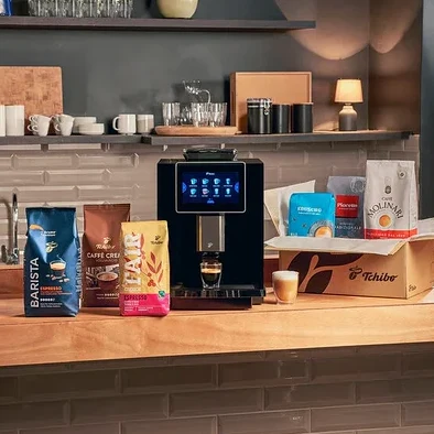 Auf einer Küchentheke stehen Kaffeebohnenpackungen und eine Tchibo-Kaffeemaschine mit einer Tasse Kaffee darunter.
