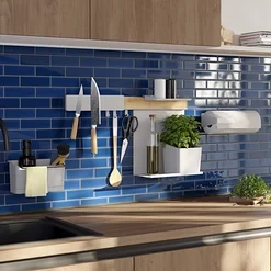 Küche mit Holzarbeitsplatte, schwarzem Spülbecken und Wasserhahn. Blaue Fliesenrückwand mit weißen Wandorganisatoren, Messern und Kräutern.