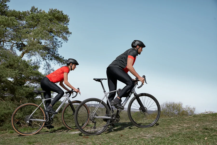 Zwei Radfahrer fahren auf ihren Fahrrädern bergauf. Sie tragen Radtrikots, Fahrradhosen und Fahrradhelme.