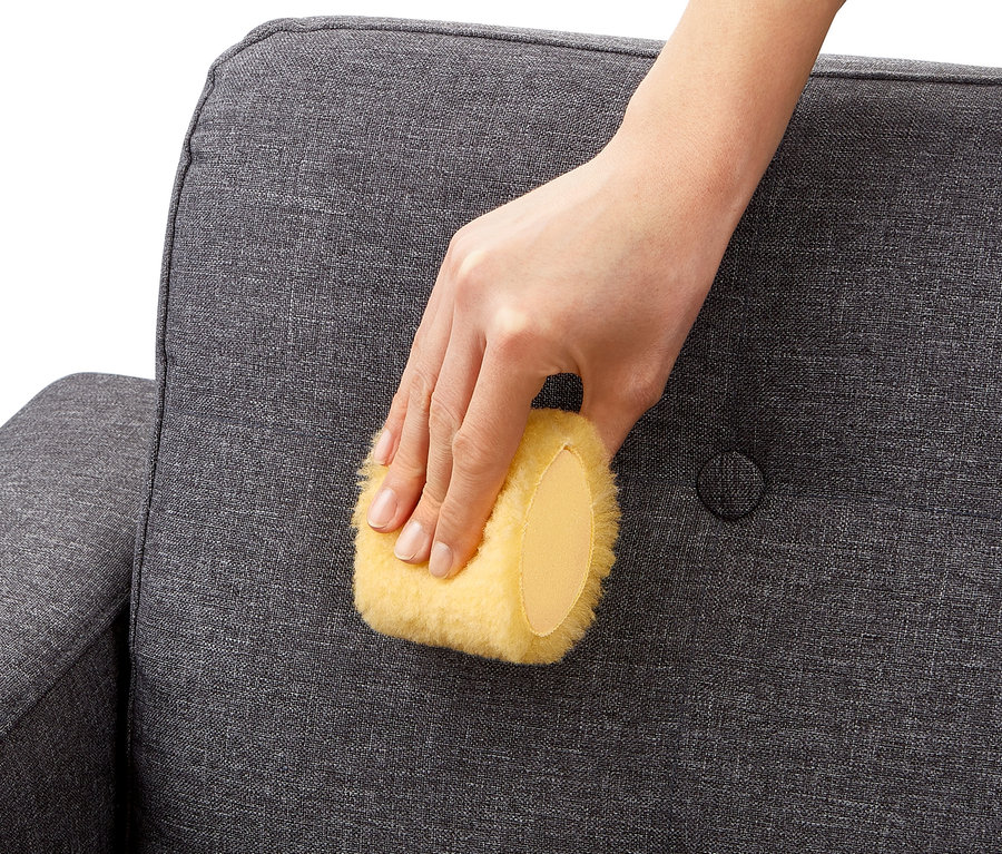 Eine Hand benutzt eine Fleckenmaus, um ein graues Sofa zu reinigen.