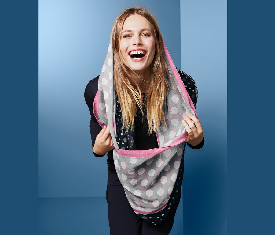Lächelnde Frau hält Loop-Schal mit Punkten über dem Kopf.