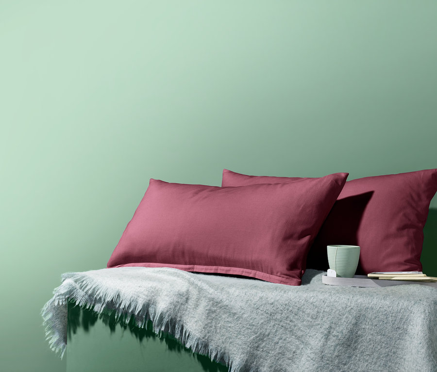 Zwei Biber-Kopfkissenbezüge liegen auf einer grauen Decke neben einer Tasse vor einem grünen Hintergrund.