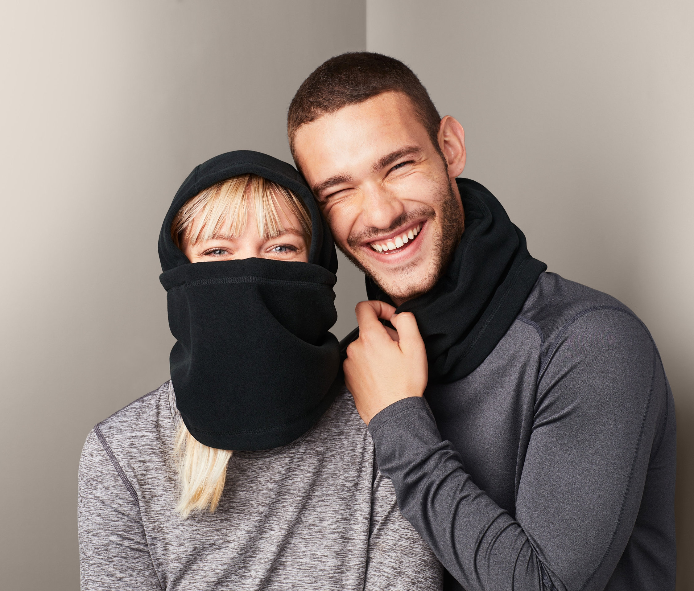 Eine blonde Frau und ein Mann lächeln und tragen Microfleece-Sturmhauben.