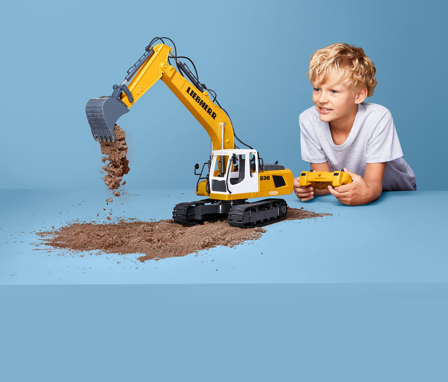 Ein Junge spielt mit einem Jamara-Bagger »Liebherr R 936« und steuert ihn mit einer Fernbedienung.