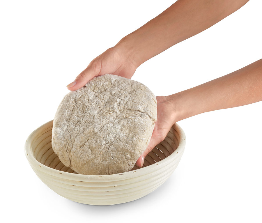 Zwei Hände legen einen Teigling in ein rundes Gärkörbchen.