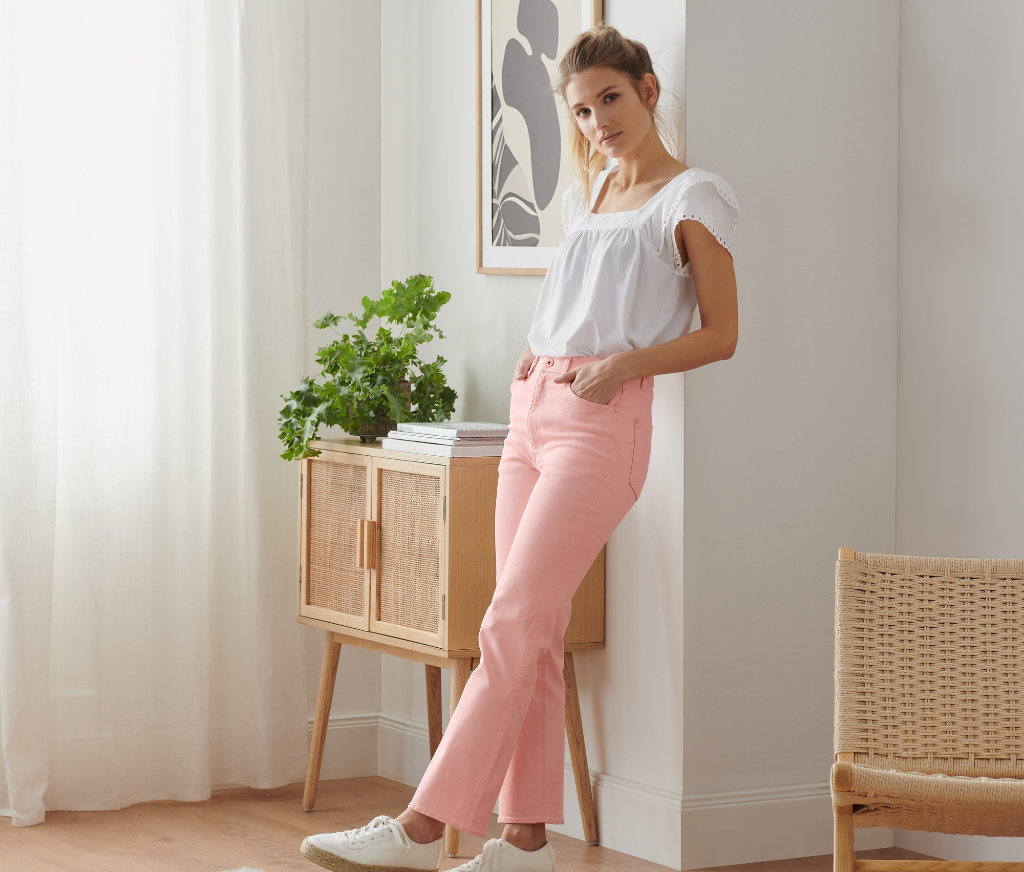 Frau lehnt an Wand und trägt eine rosafarbene Schlaghose.