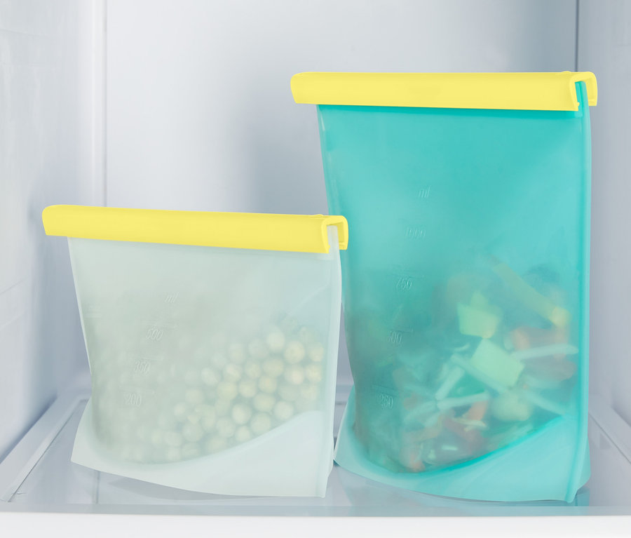 Zwei Snackbeutel mit gelben Verschlüssen stehen im Kühlschrank. Ein Beutel ist mit Erbsen und der andere mit geschnittenem Gemüse gefüllt.