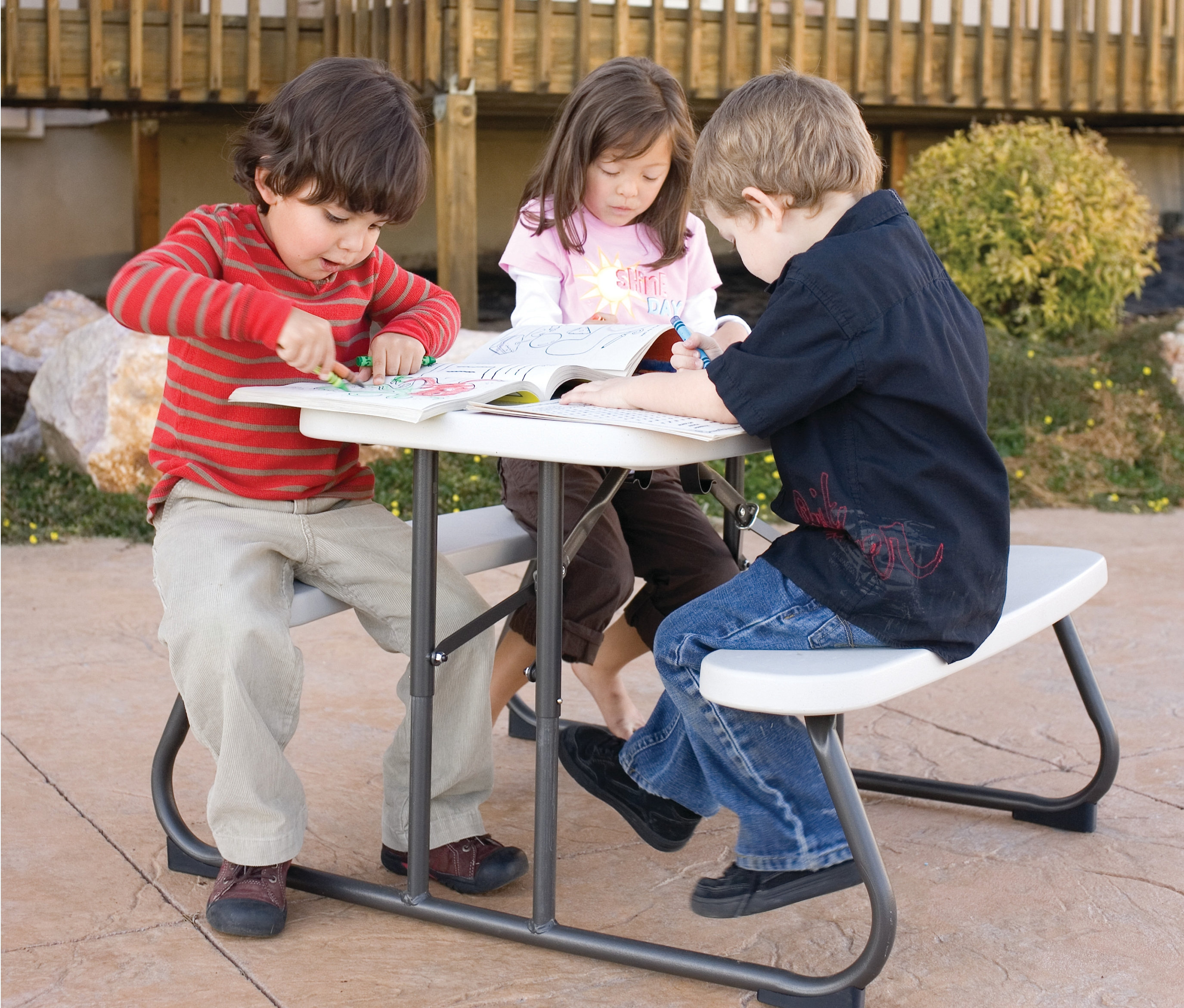 Drei Kinder sitzen an einem hellgrauen LIFETIME Kinder-Picknicktisch und malen in Malbüchern.