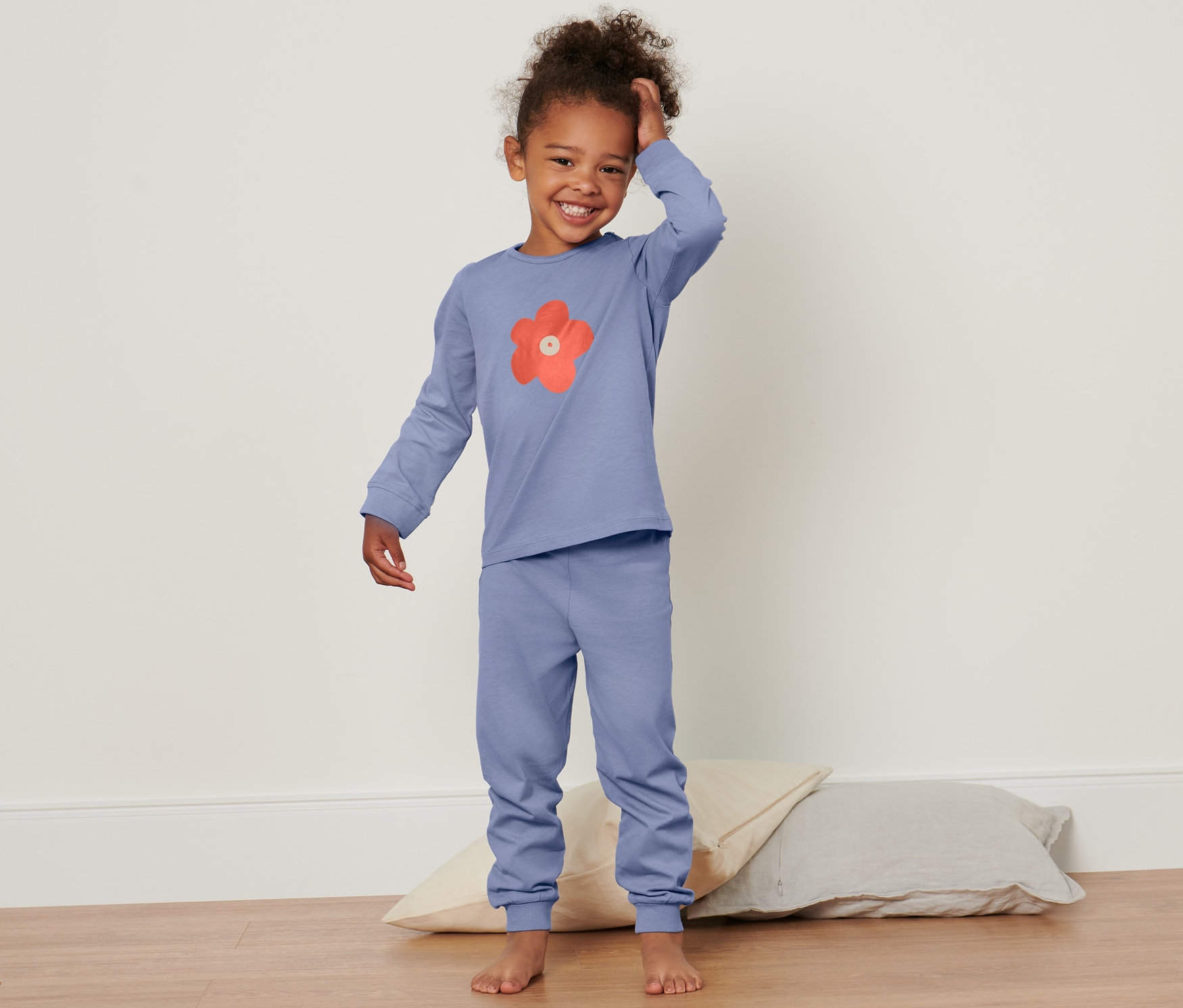 Lächelndes kleines Mädchen im Kleinkind-Pyjama posiert auf dem Boden mit Kissen.