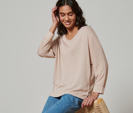 Frau sitzt auf Korbsessel und trägt Fledermausshirt.