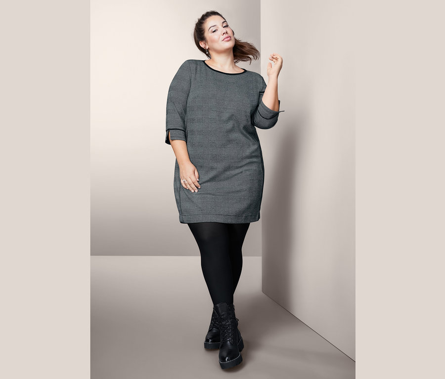 Frau posiert in Sweatkleid mit 3/4-Arm, schwarzer Strumpfhose und schwarzen Stiefeln.