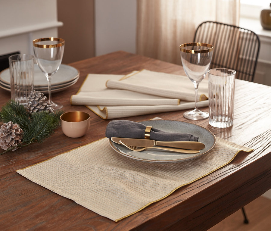 Auf einem Holztisch liegen vier beige Platzsets.
