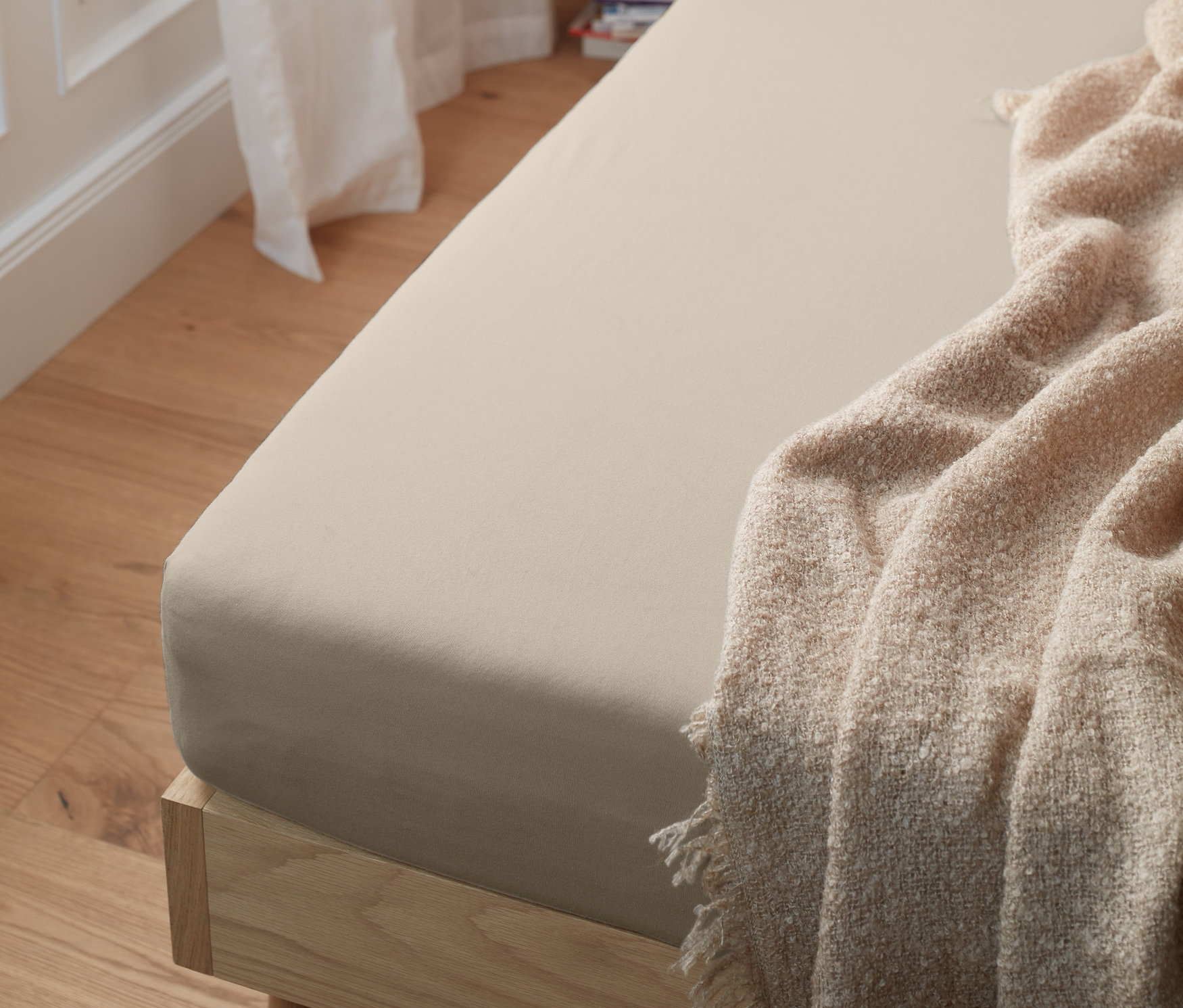 Ein cremefarbenes Jersey-Spannbettlaken auf einem Bett.