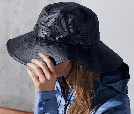 Frau sitzt auf Bank, trägt Unisex-Regenhut.