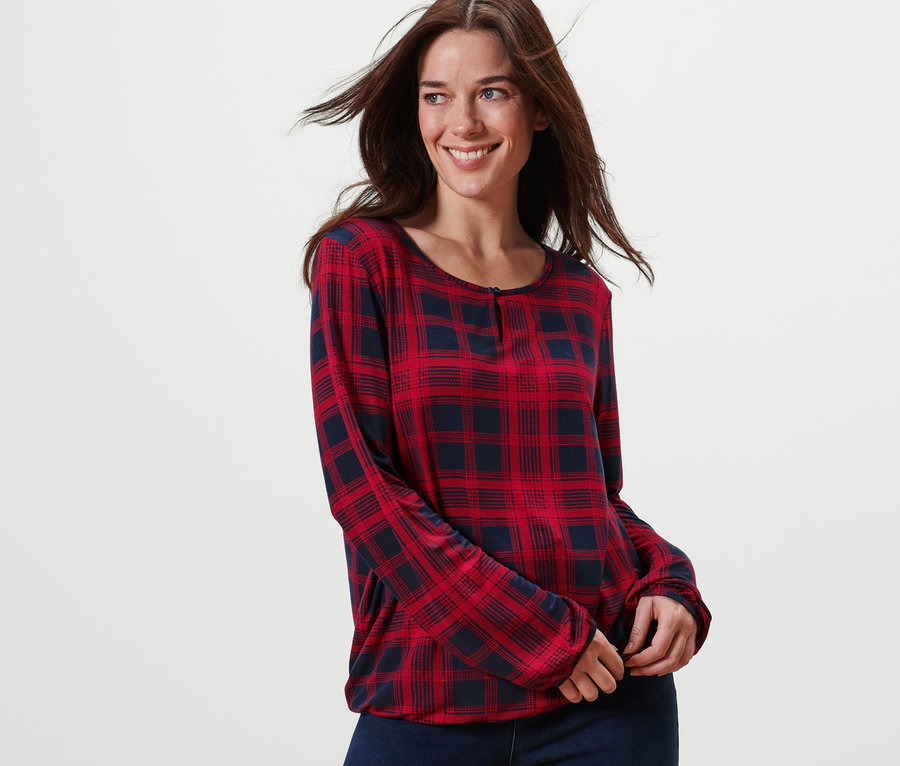Lächelnde Frau posiert in einem karierten Blusenshirt.
