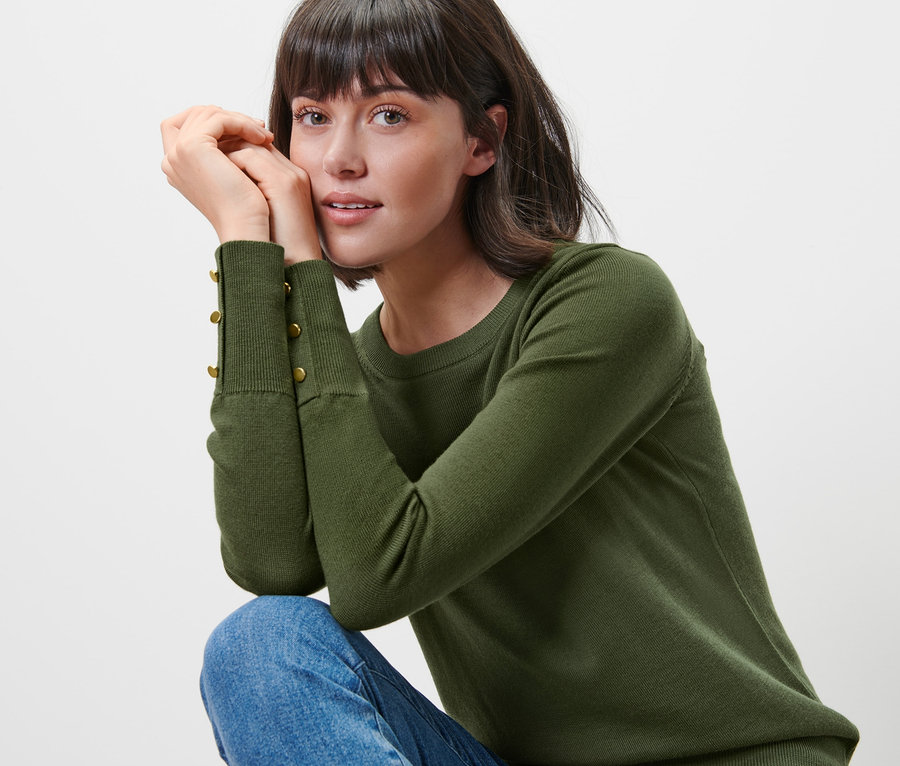Frau posiert in grünem Feinstrickpullover mit Merinowolle und blauen Jeans.