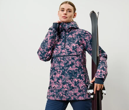 Frau posiert in Halfzip-Skijacke mit Alloverprint und hält Ski.