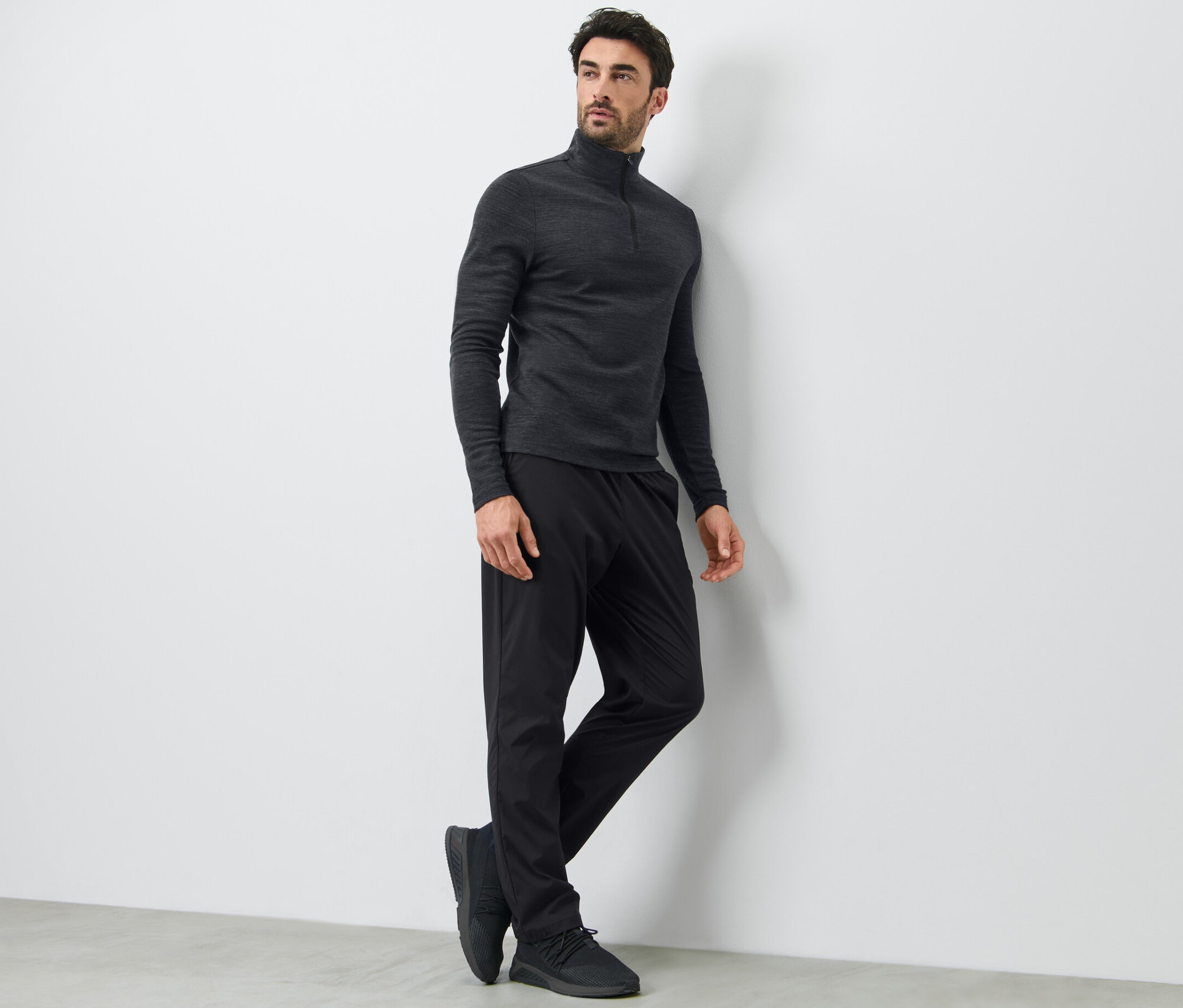Mann lehnt an einer Wand und trägt eine schwarze Funktionshose und ein langärmeliges Oberteil.