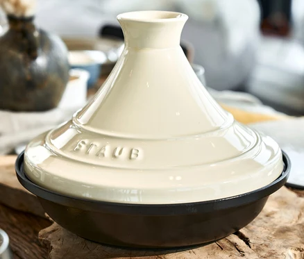 Nahaufnahme einer STAUB Gusseisen-Tajine, creme, 28 cm auf einem Holztisch.