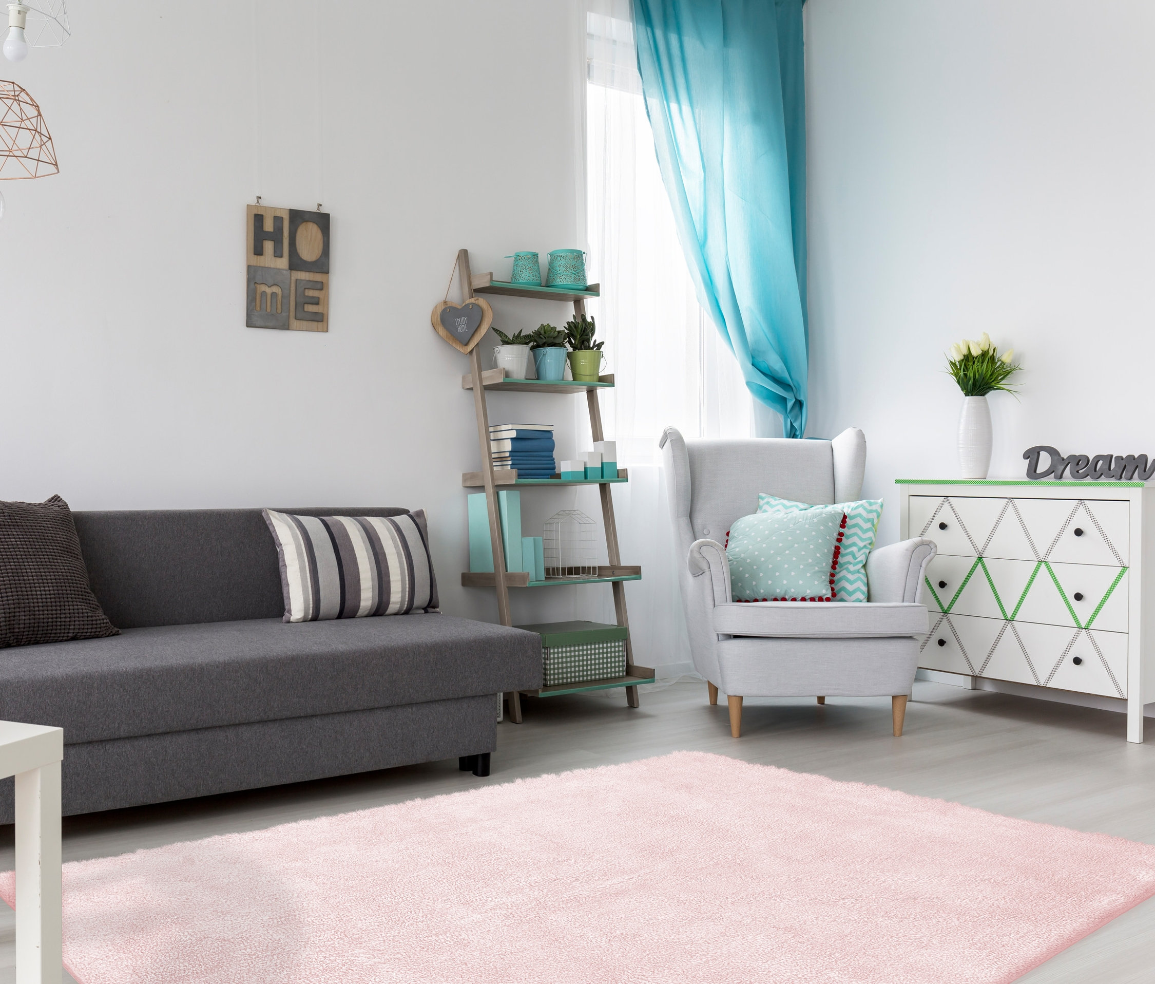 Wohnzimmer mit grauem Sofa mit Kissen, hellrosa Kayoom Bali Teppich und grauem Sessel.