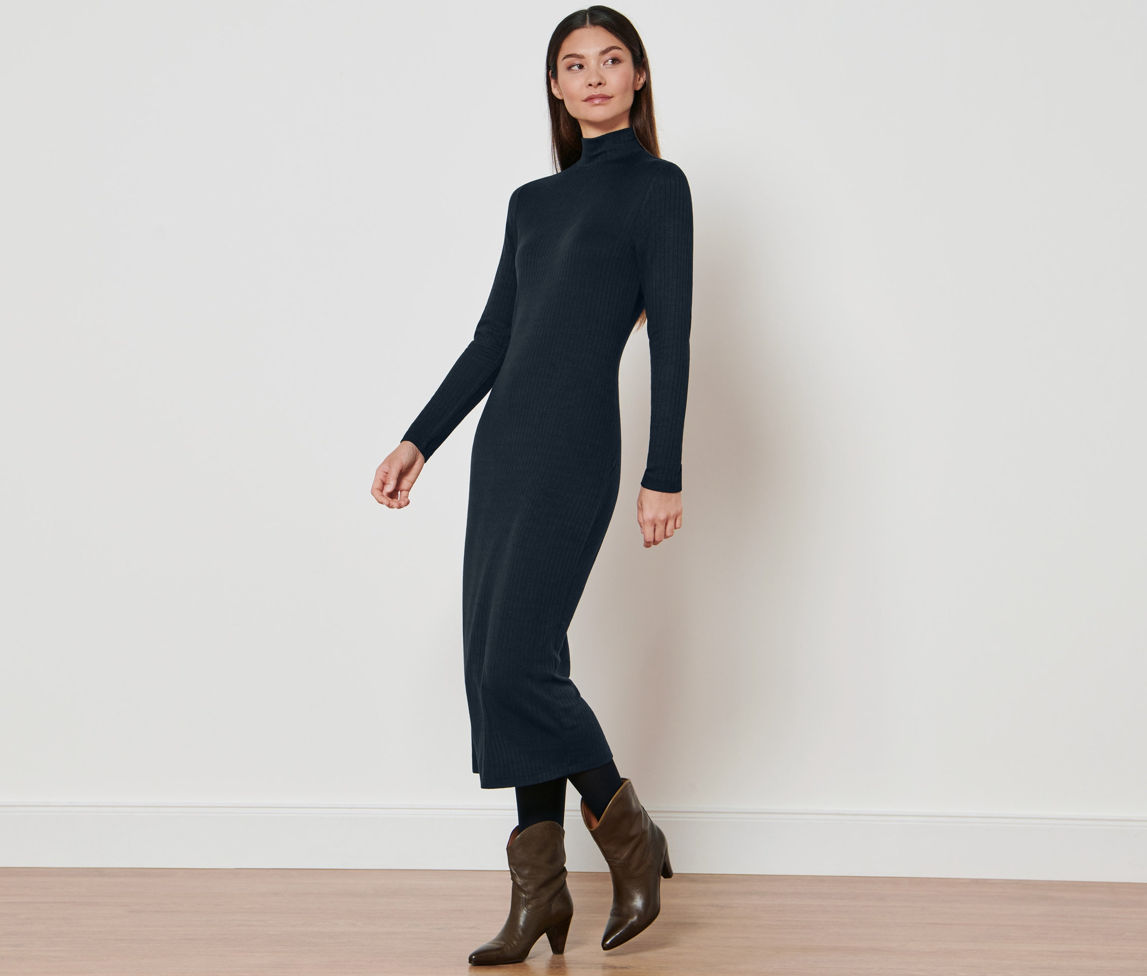 Frau posiert in einem Jerseykleid mit Rollkragen und braunen Cowboystiefeln.