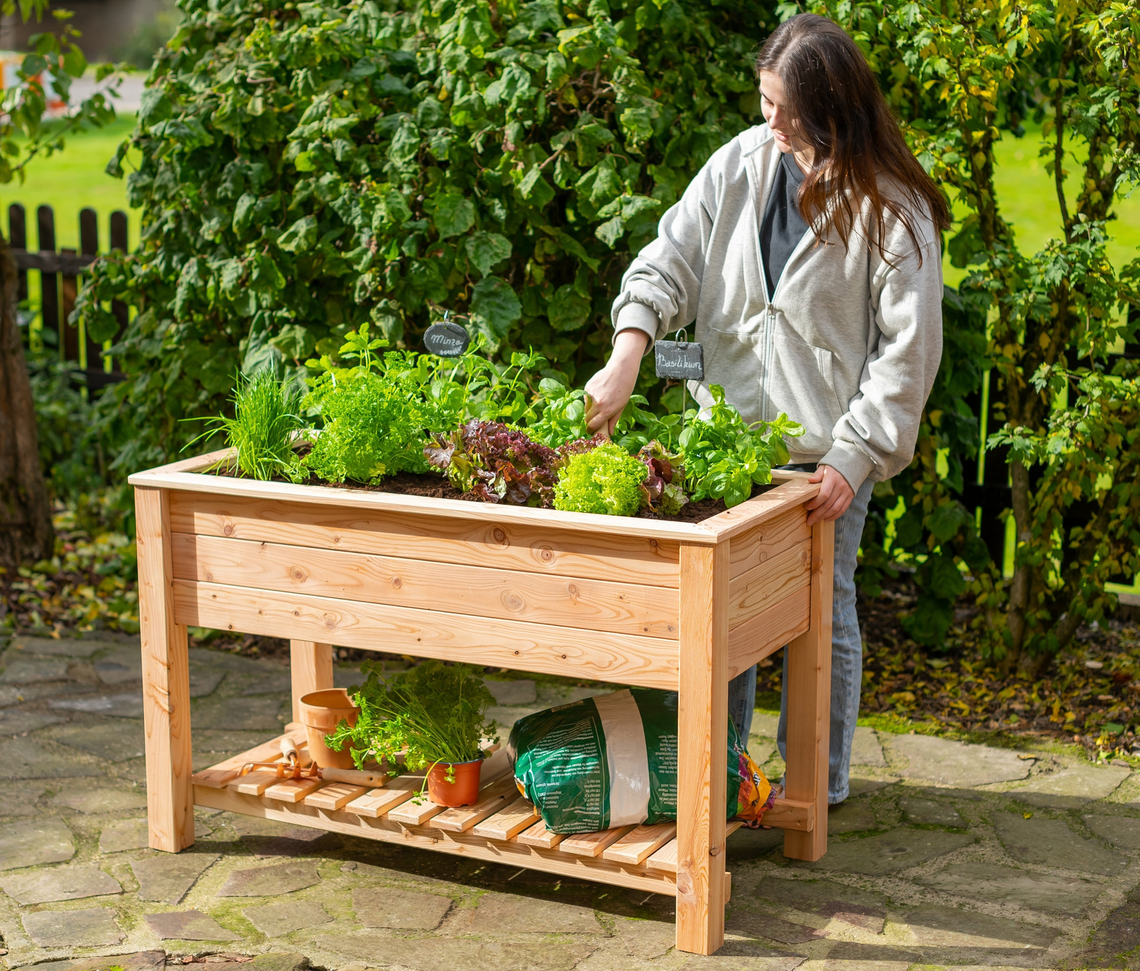 Eine Frau pflegt Pflanzen in einem Stelzenhochbeet mit Boden.