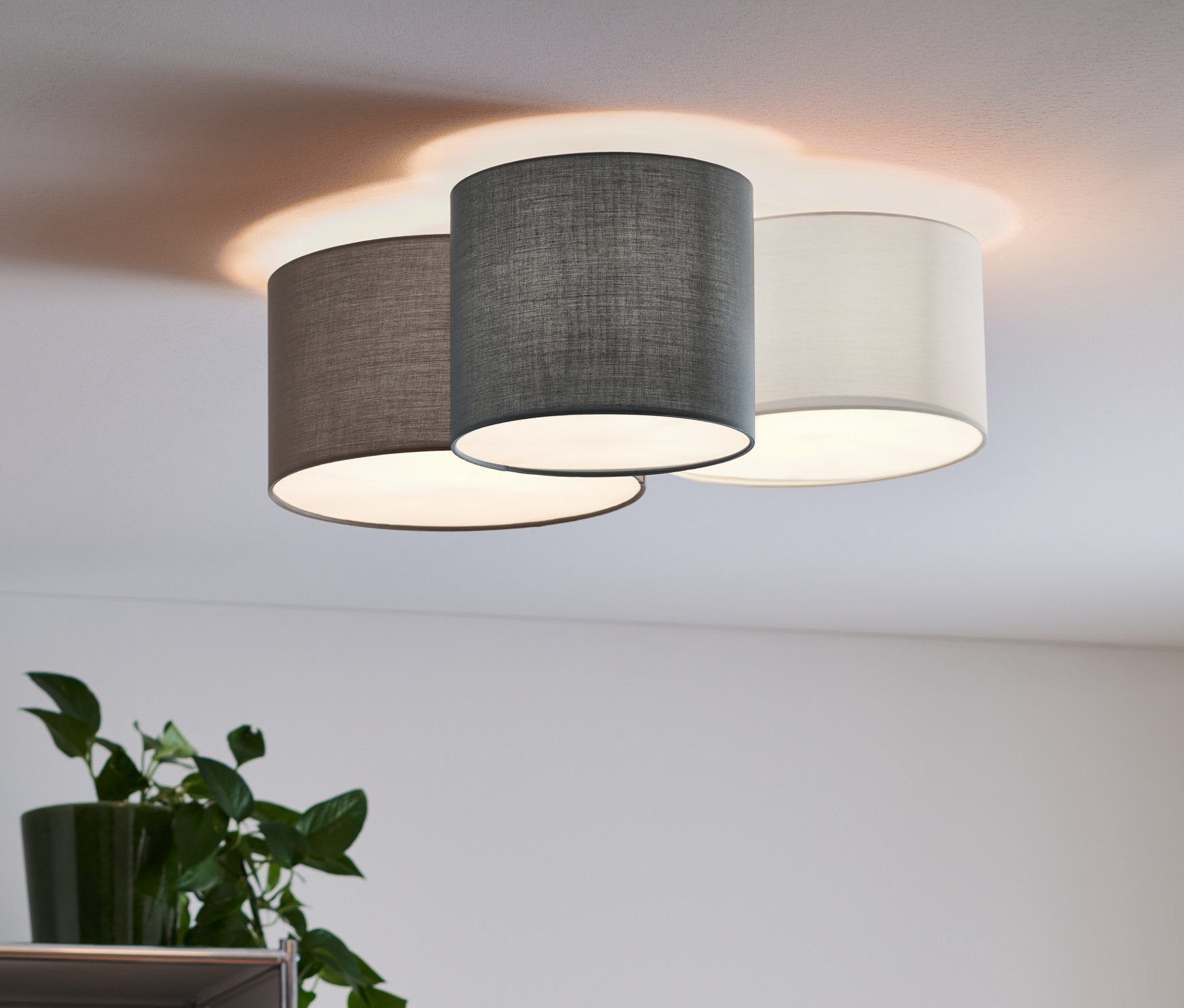 Eine Deckenleuchte mit Textilschirm, 3-flammig, beleuchtet den Raum.