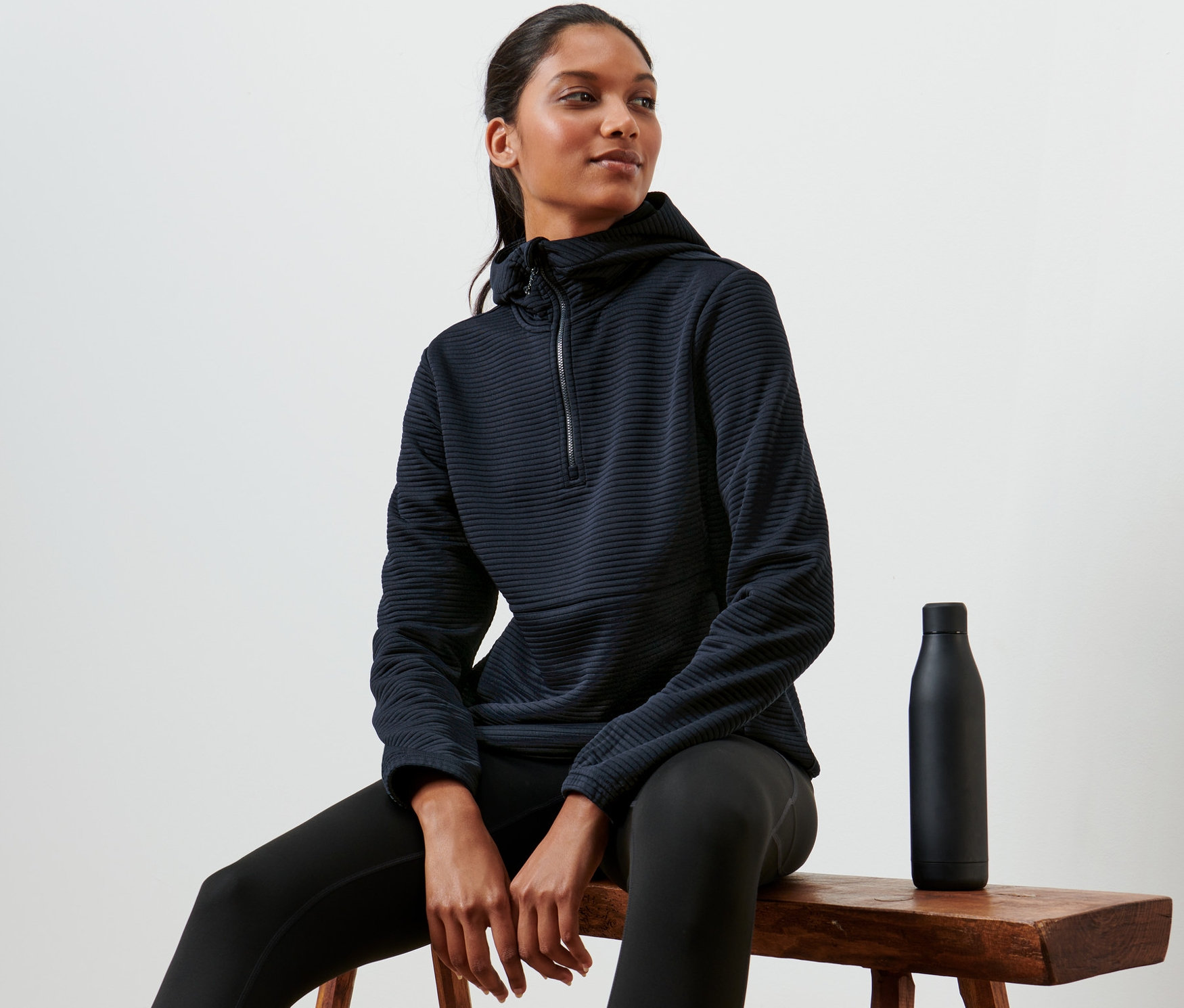 Frau sitzt auf einem Hocker und trägt einen Kapuzenpullover.