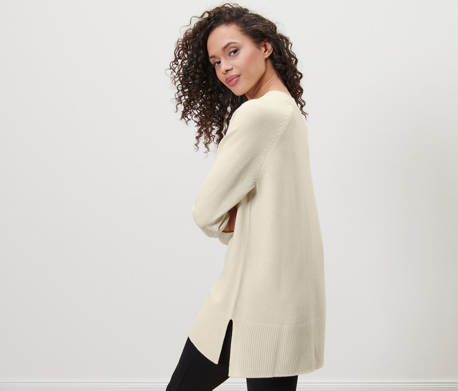 Frau posiert in langem Strickpullover, cremeweiß.