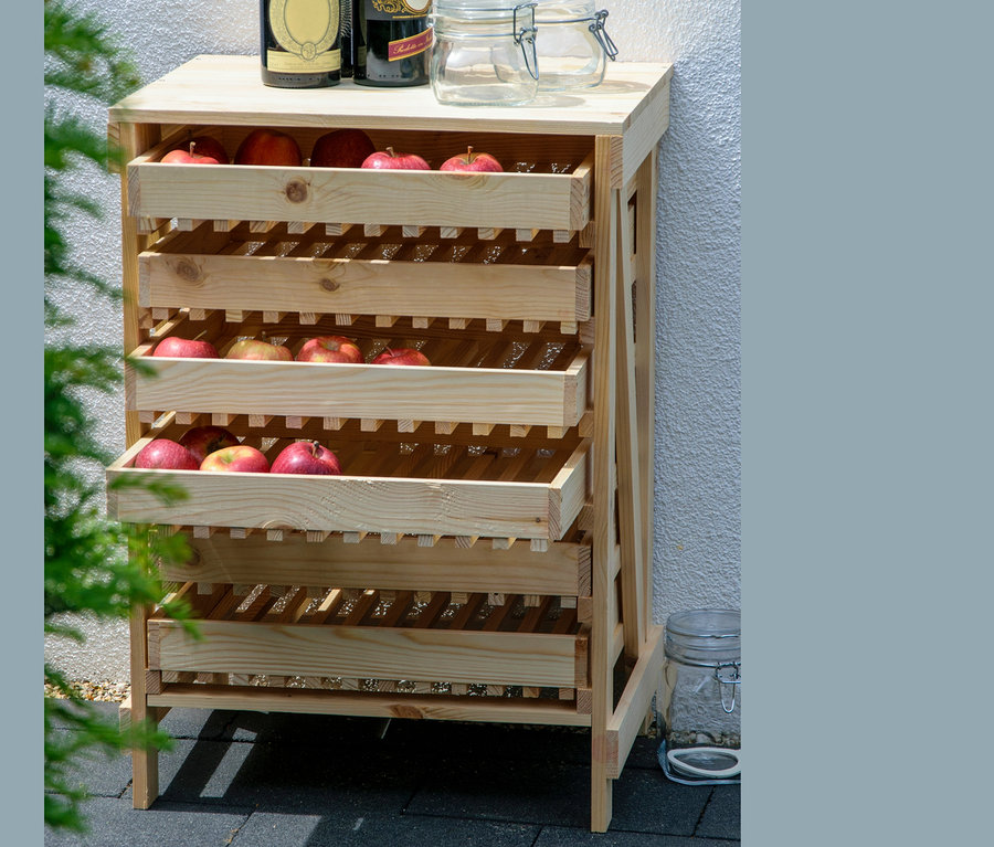 Ein Dobar Vorratsregal aus Holz mit drei Schubladen voller roter Äpfel, auf der obersten Ablage stehen Weinflaschen und Gläser.