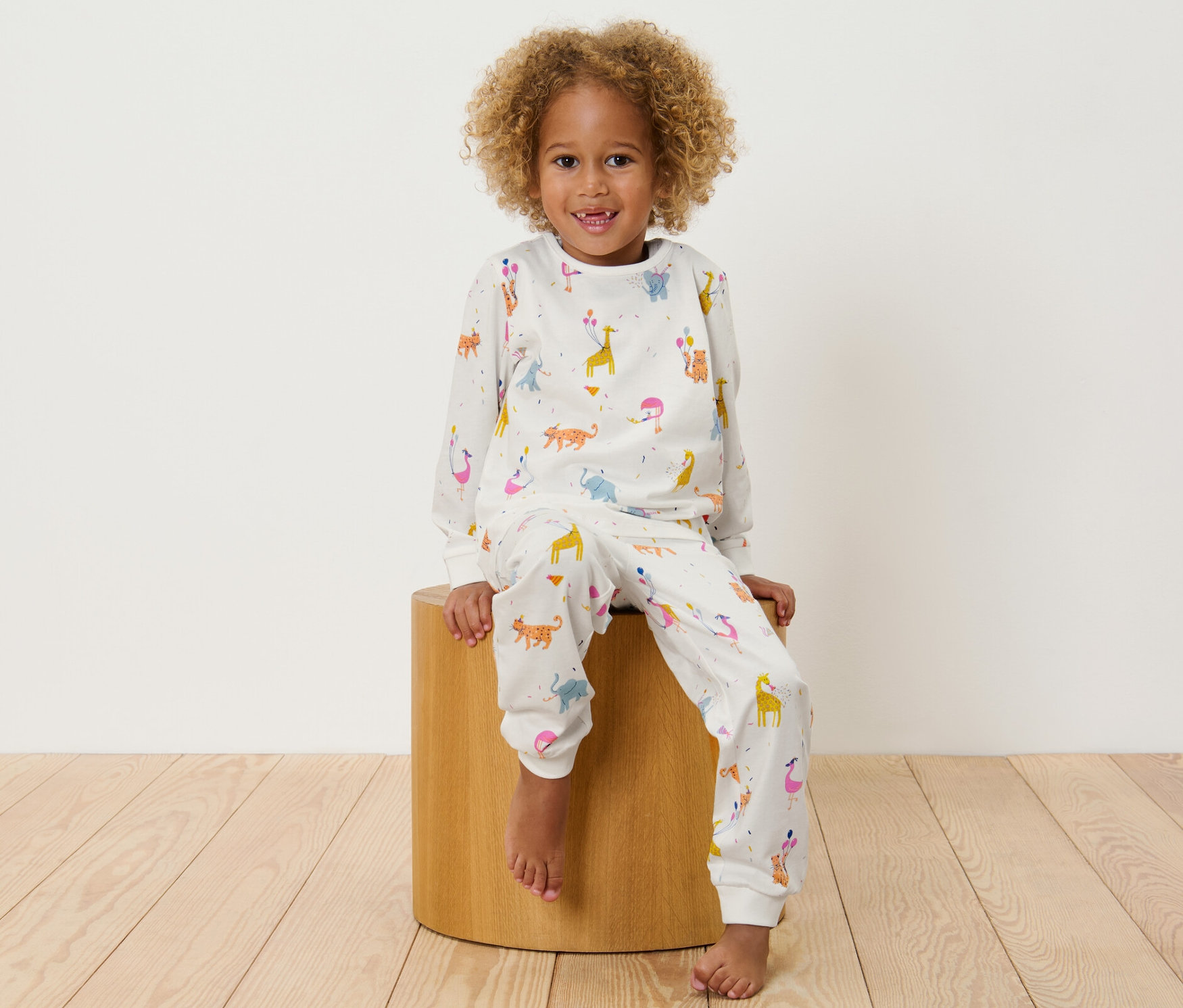 Ein Kind sitzt auf einem Holzhocker und trägt einen Kinder-Pyjama mit Tiermotiven.