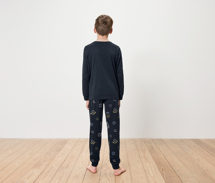 Junge steht mit dem Rücken zur Kamera und trägt einen dunkelblauen Schlafanzug mit langen Ärmeln und Hosen mit Smiley-Gesichtern.