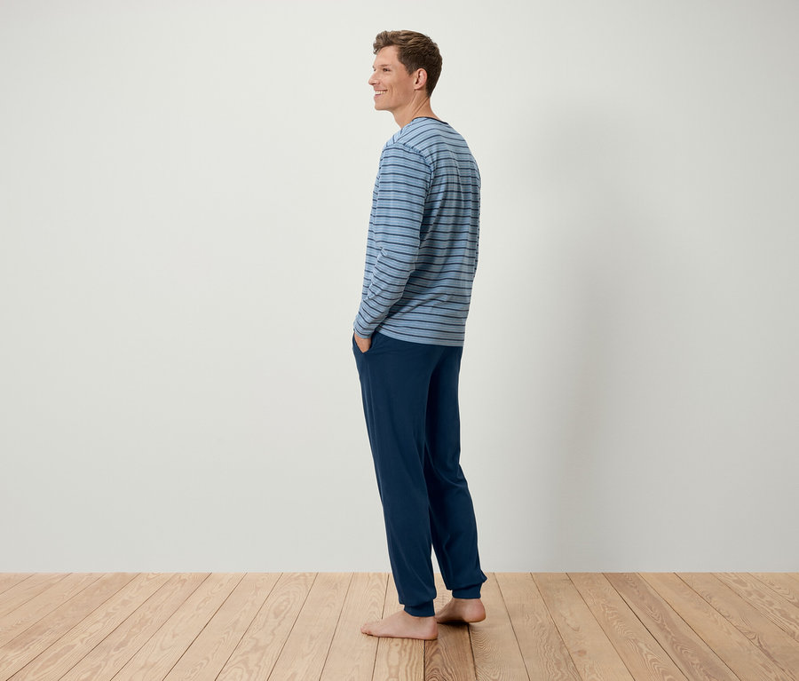 Mann steht seitlich und trägt ein blau gestreiftes Langarmshirt und dunkelblaue Hosen.
