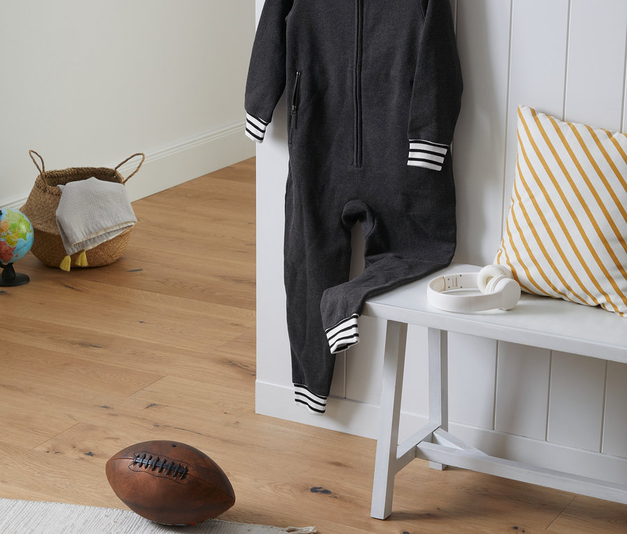 Ein dunkelgrauer Kinder-Loungeoverall hängt an einem weißen Kleiderbügel neben einer weißen Bank.