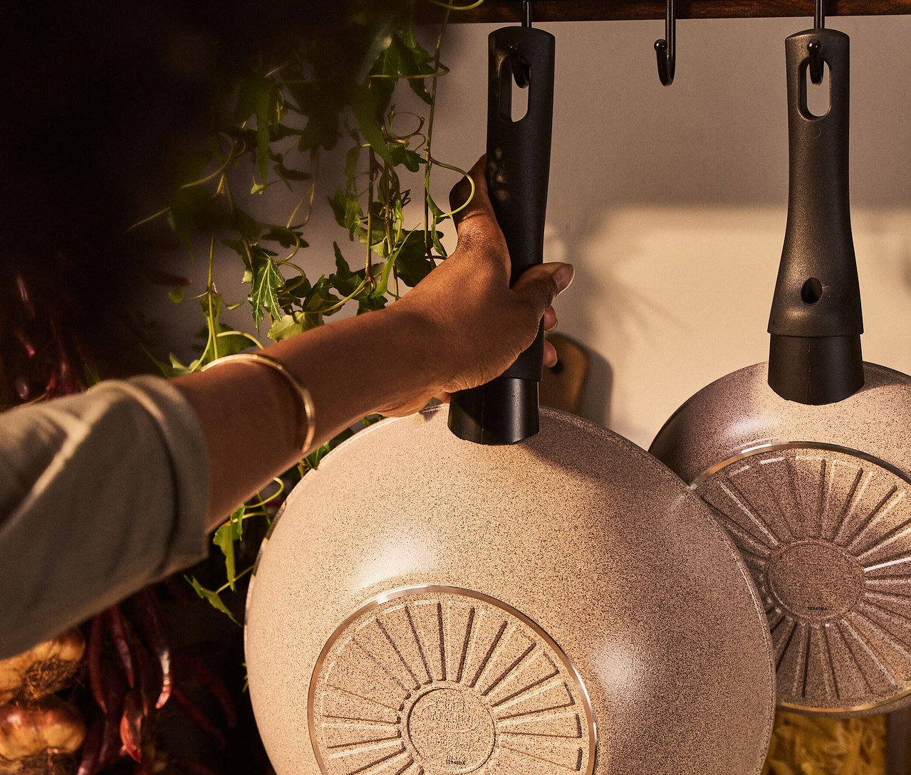 Eine Hand greift nach einem BALLARINI Ledro Wok (28 cm), der an einer Stange hängt.